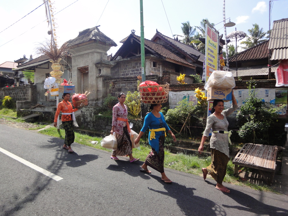 Local women return home after the day's shop, wandering the road under festive penjor decorations.